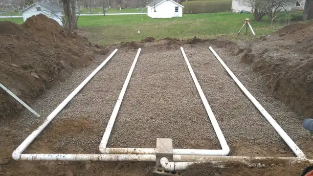 Finished septic leach field with distribution lines set in gravel beside a lawn