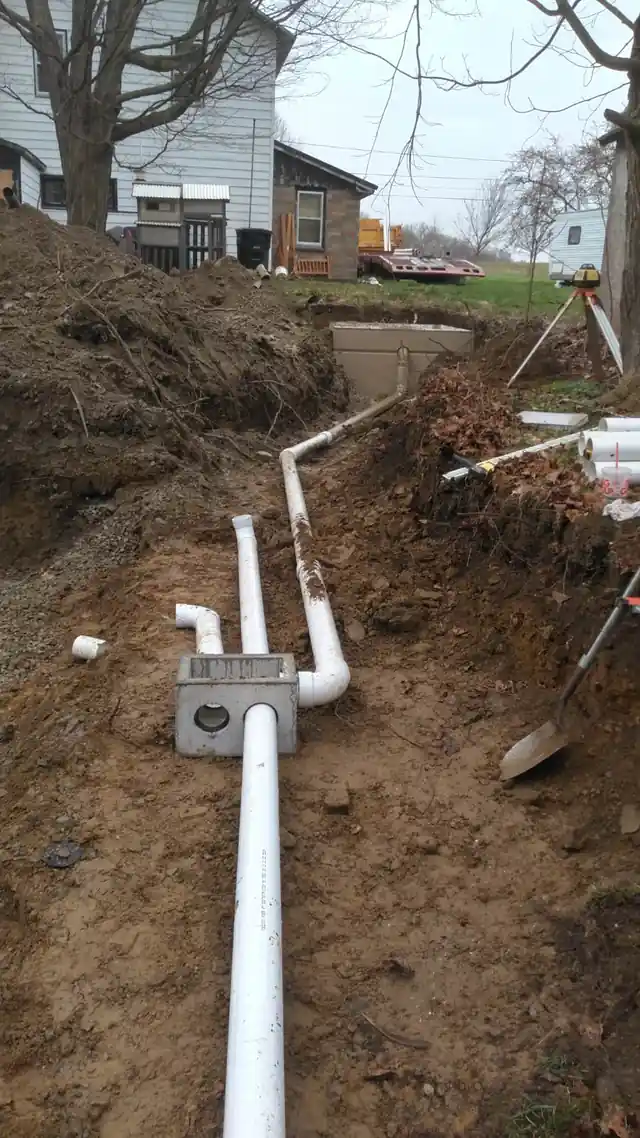 Septic line trenching and riser install alongside a residential foundation